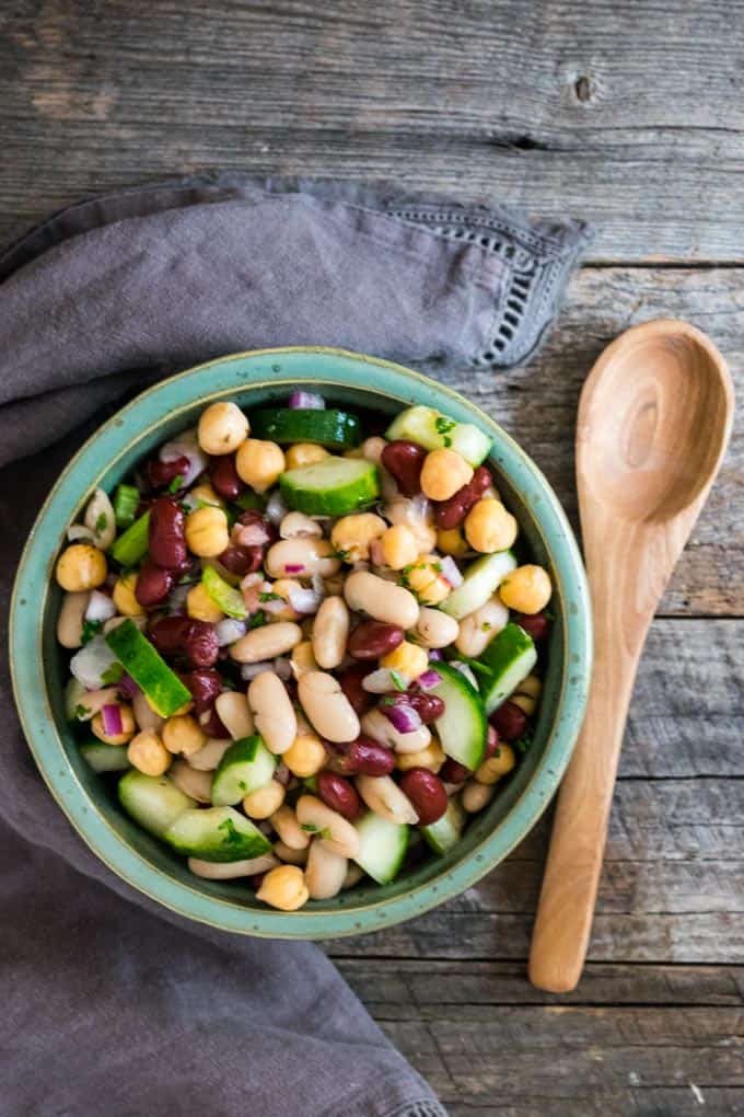 three bean salad in green bowl on table with wooden spoon.