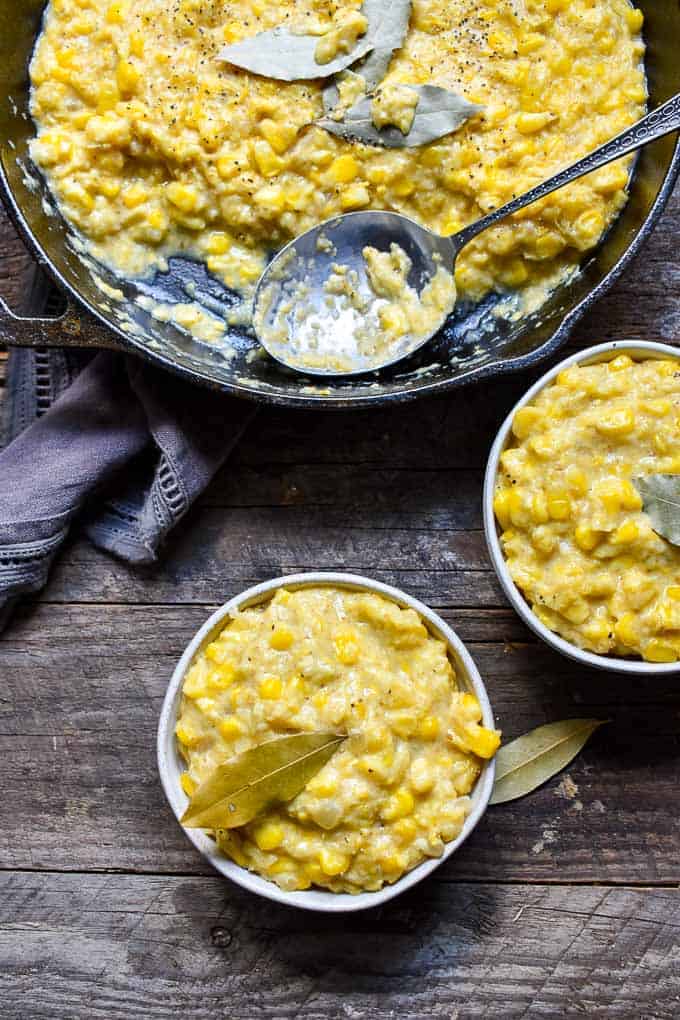 Homemade Vegan Creamed Corn on table with bowls and cast iron skillet