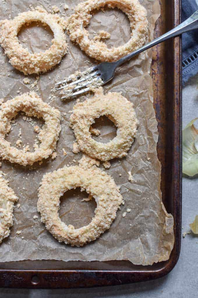 Crunchy baked onion rings battered on baking pan.
