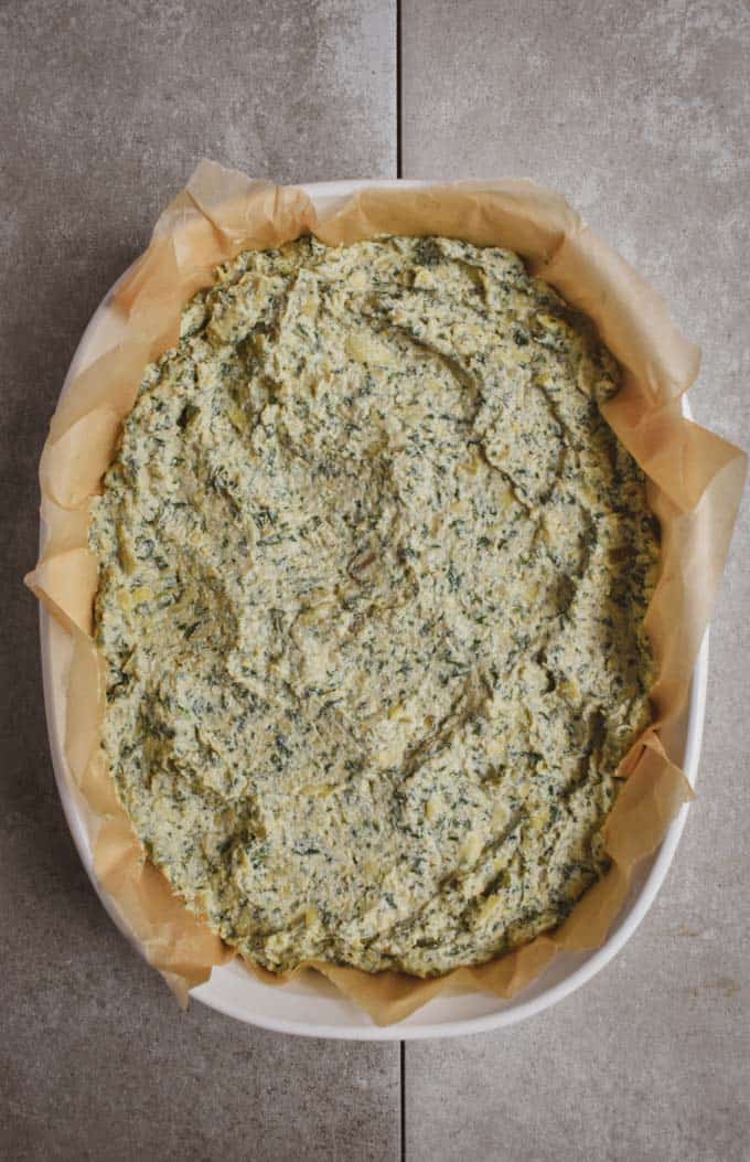 Creamy vegan spinach artichoke dip ingredients in baking dish wit parchment paper.