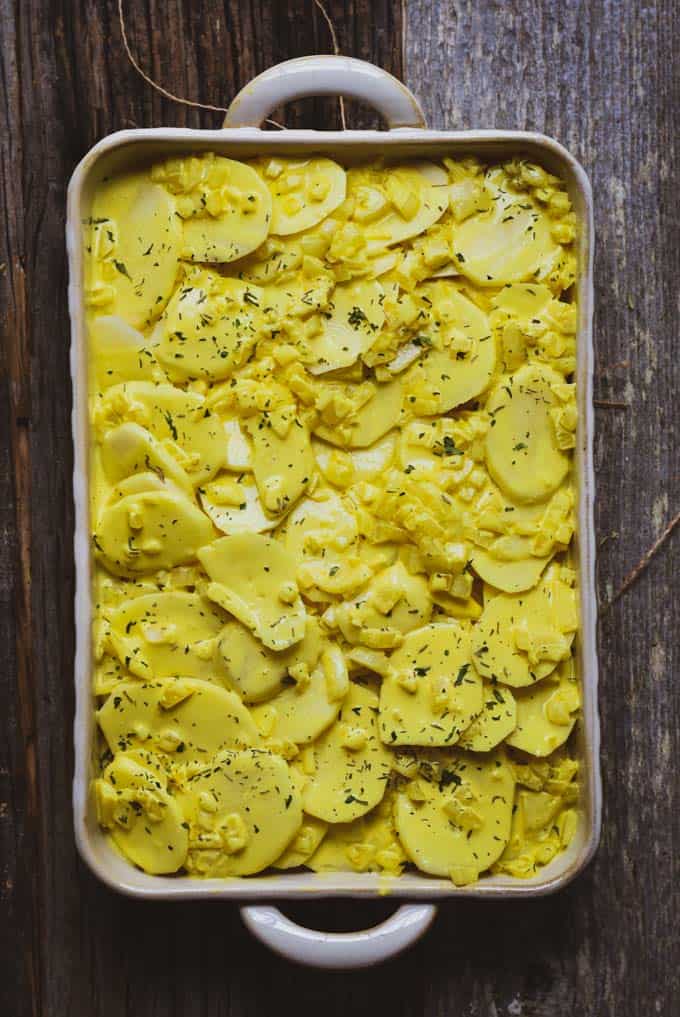 Creamy vegan scalloped potatoes in baking dish with sauce and onions before being cooked.