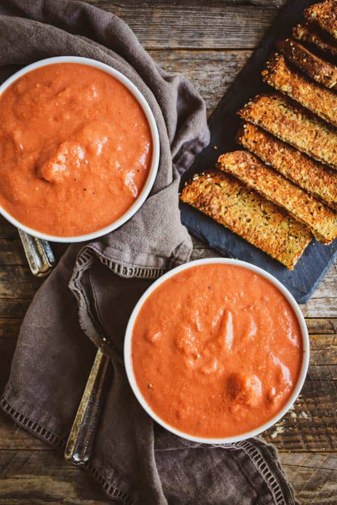 Creamy vegan tomato soup without toppings on table with bread and napkin.