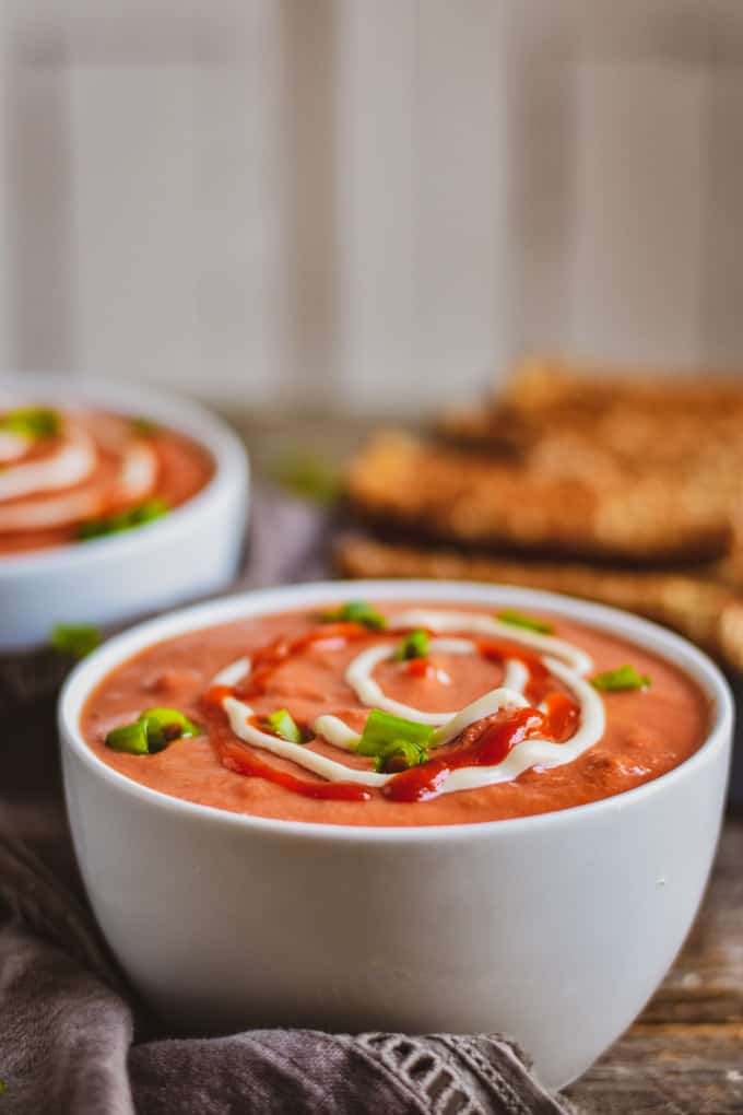 Bowl of creamy vegan tomato soup with sriracha and cashew sweet cream.