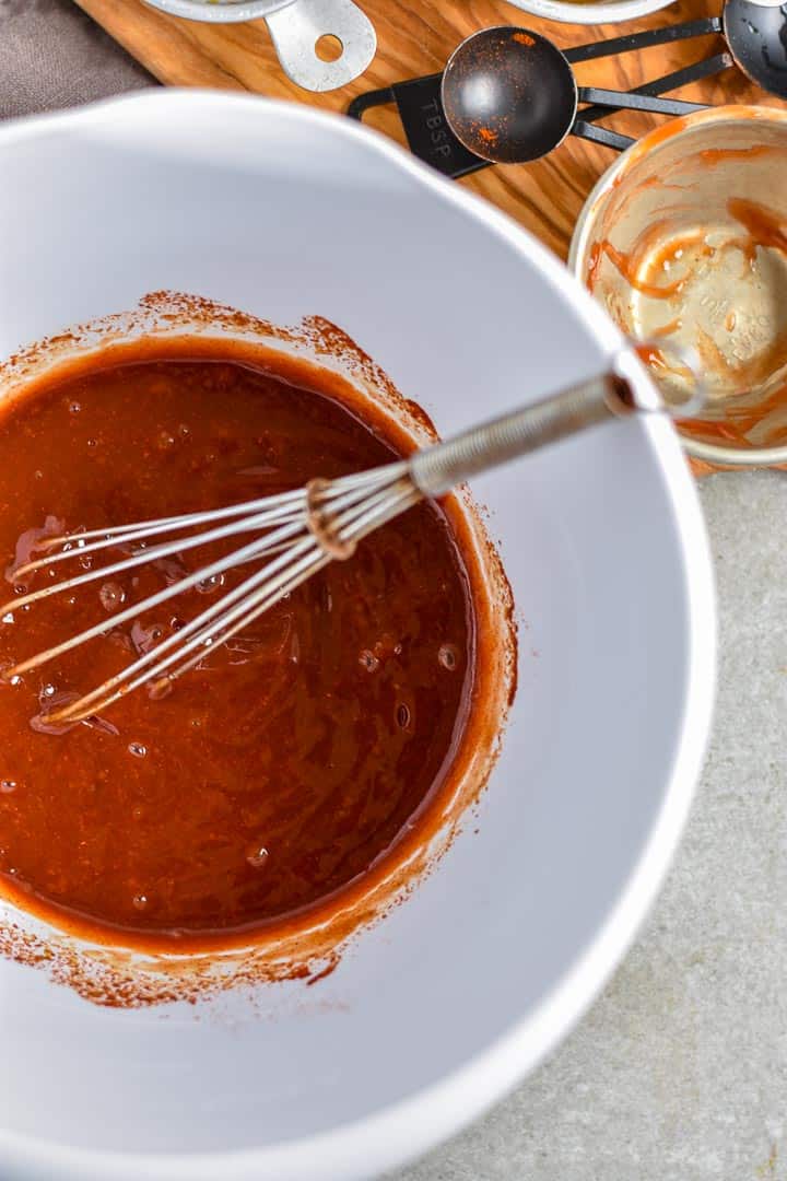 White mixing bowl with whisk and bbq sauce ingredients combined.