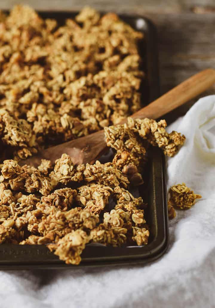 Granola with a wooden spoon in a baking sheet on white cloth.