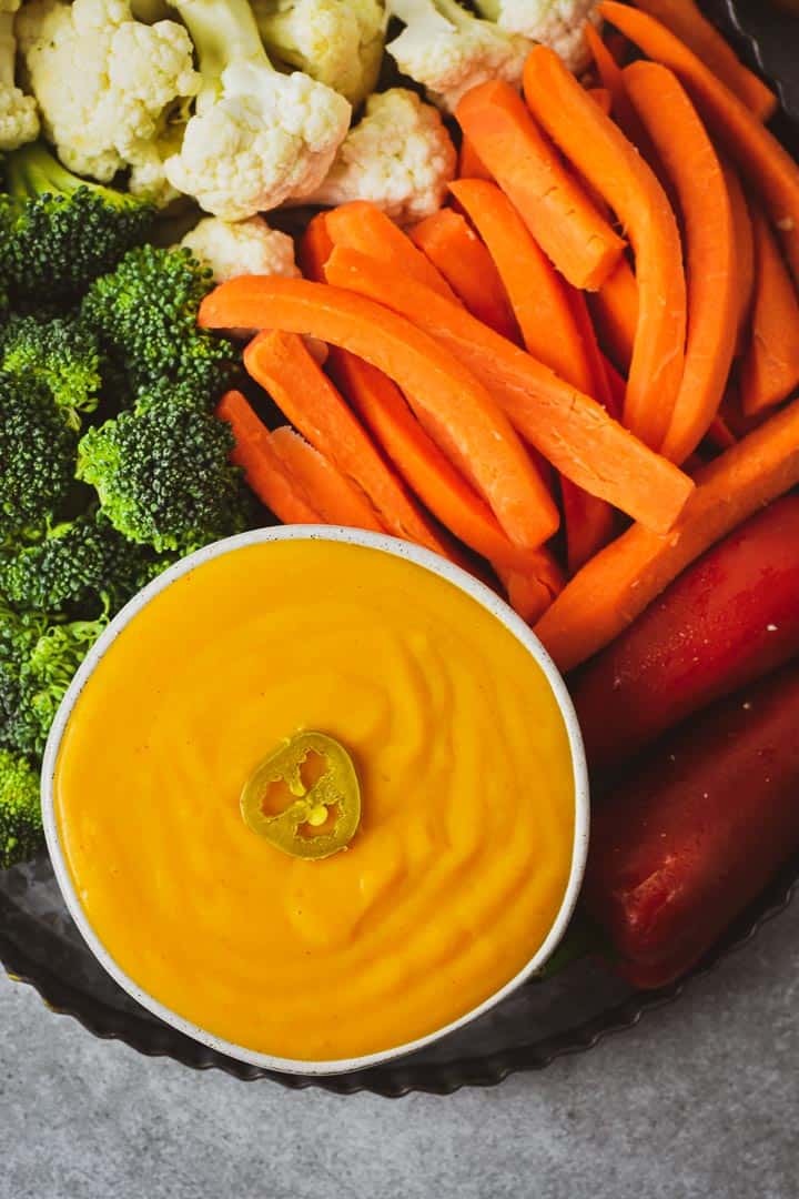 Cheese sauce on table with carrots, broccoli, carrots, and cauliflower.