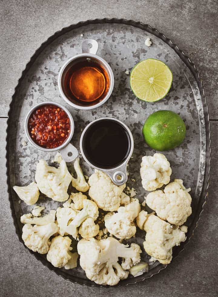 Cauliflower pieces, soy sauce, garlic sauce, maple syrup, and lime juice on serving tray.