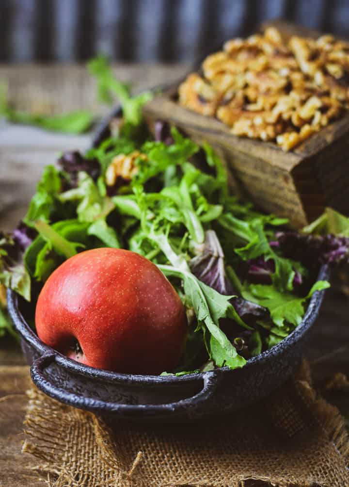 Apple in bed of salad greens with walnuts in the background.