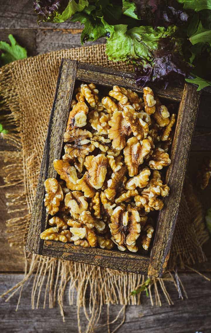 Walnuts in a wooden box on burlap with salad greens.