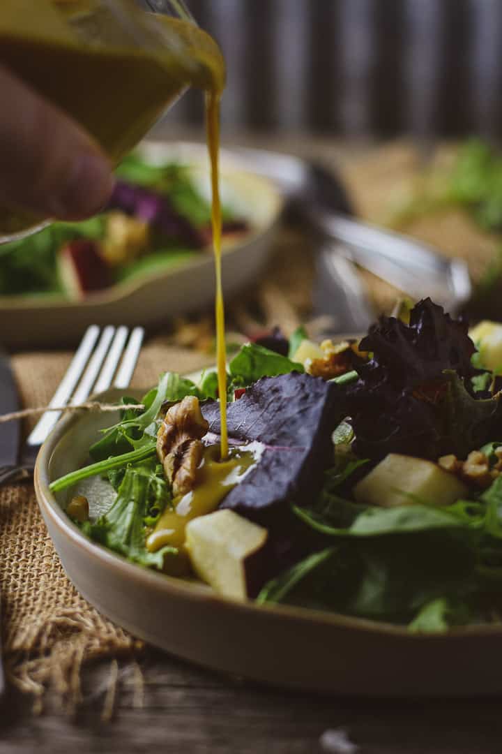 Jar of honey mustard being poured onto salad.