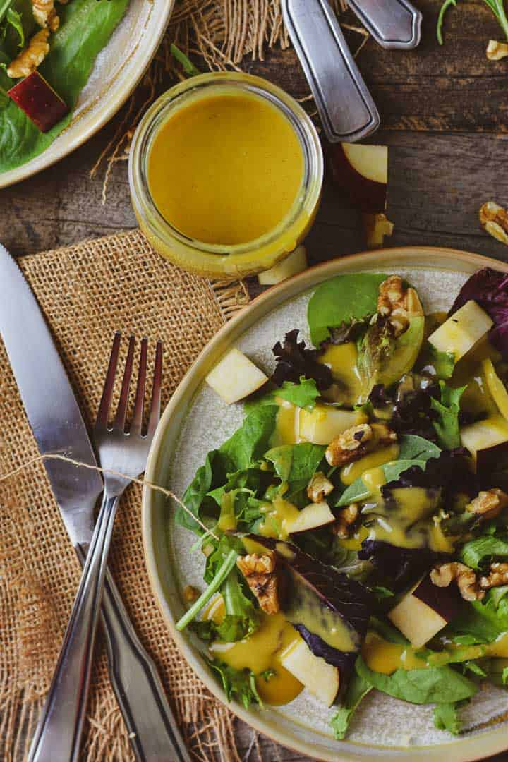 Salad with dressing on table with knife and fork and honey mustard dressing.