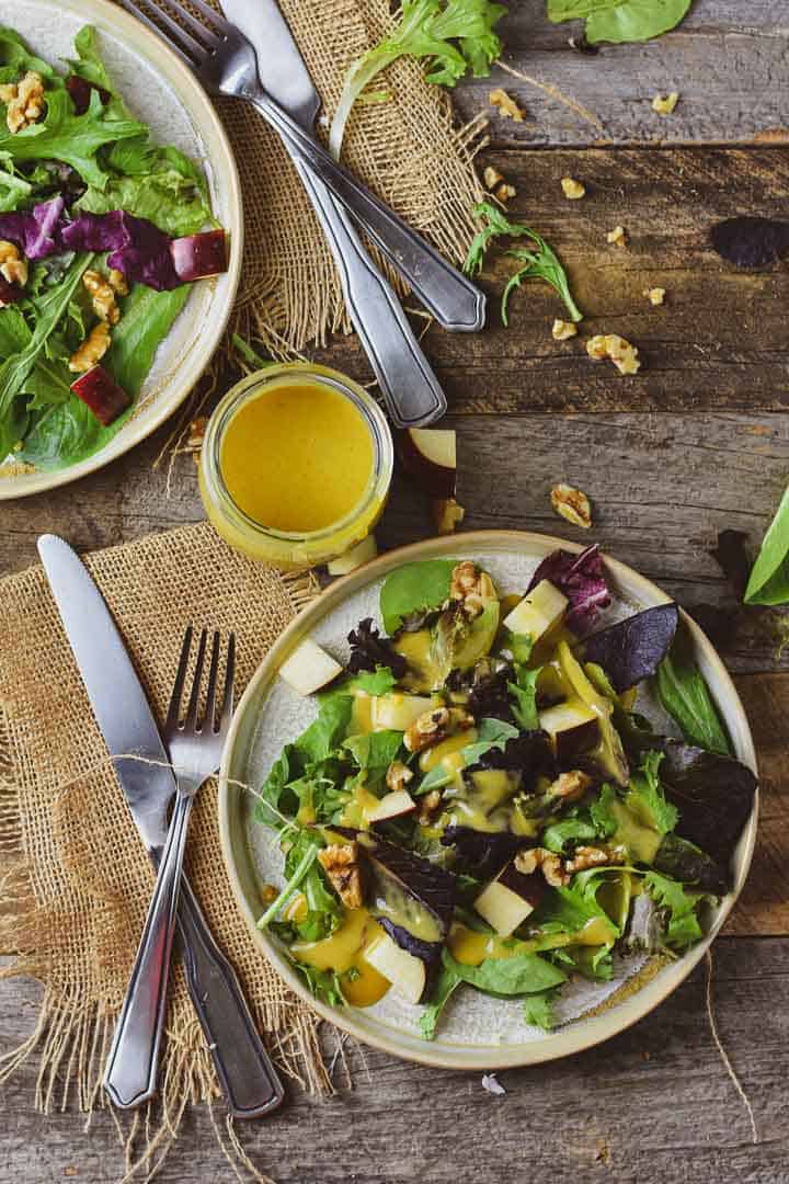 Apple walnut salad on table with honey mustard dressing and utensils.