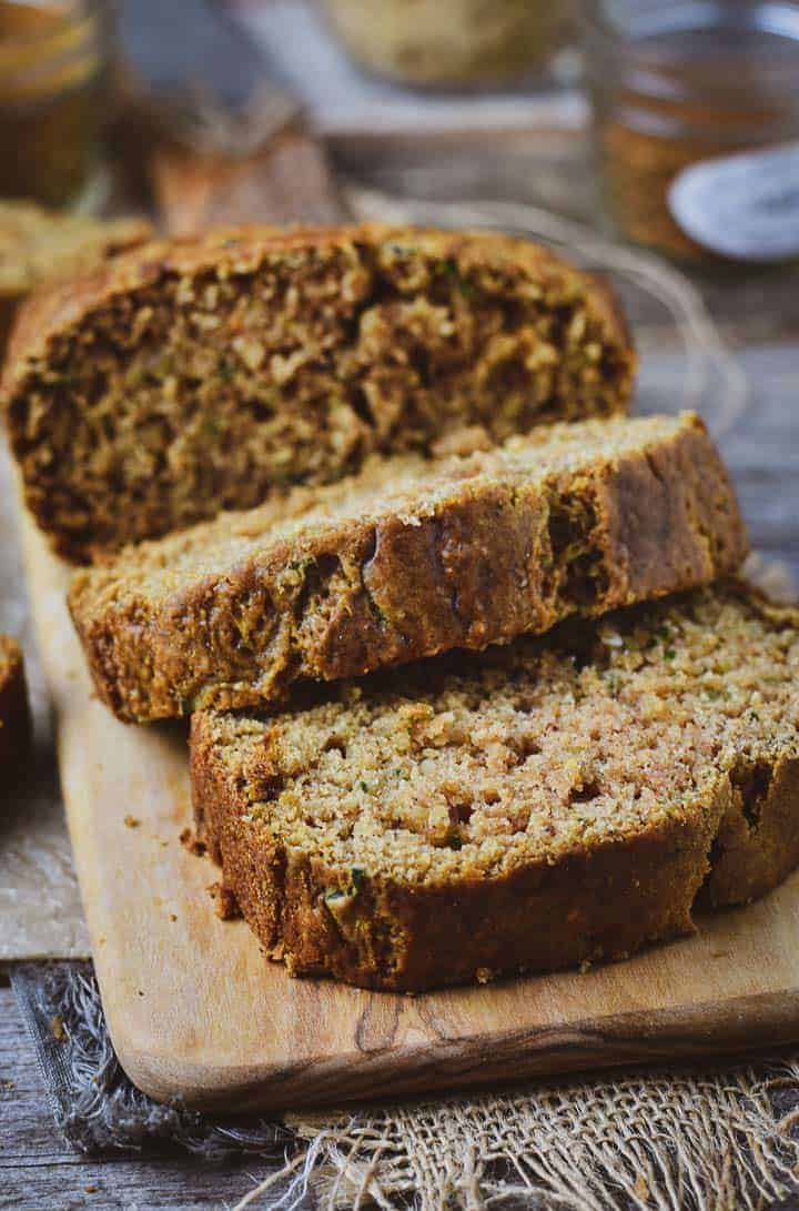 Two slices and half loaf of vegan zucchini bread on cutting board