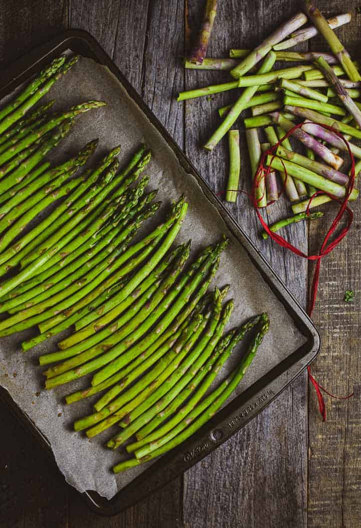 Asparagus on baking sheet and broken stems on table.