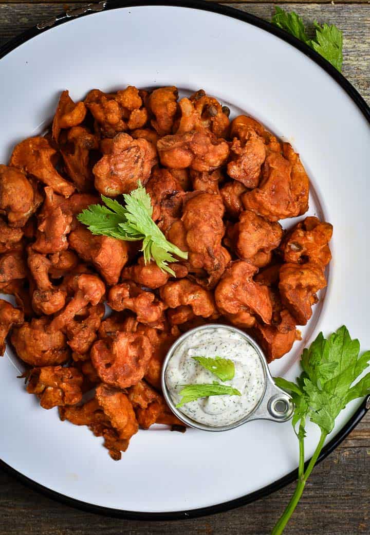 vegan buffalo cauliflower wings on white plate with ranch dressing.
