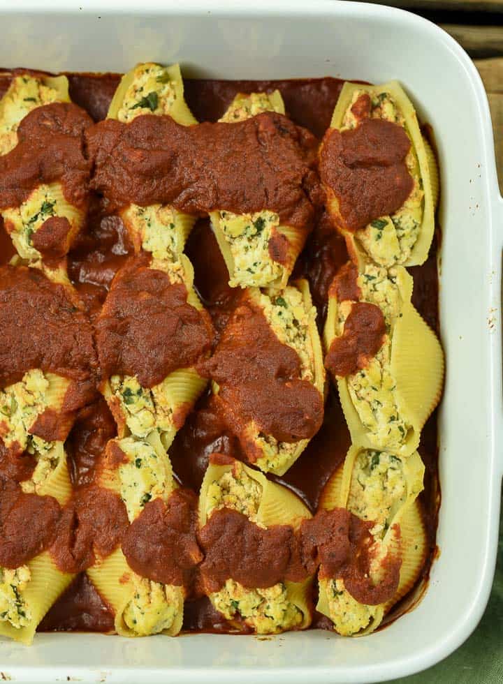 Cooked vegan stuffed shells with tofu ricotta in baking dish with pasta sauce.