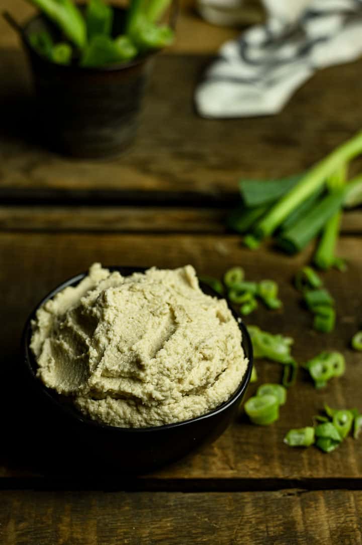 Vegan cream cheese in black bowl on table with chopped green onion.