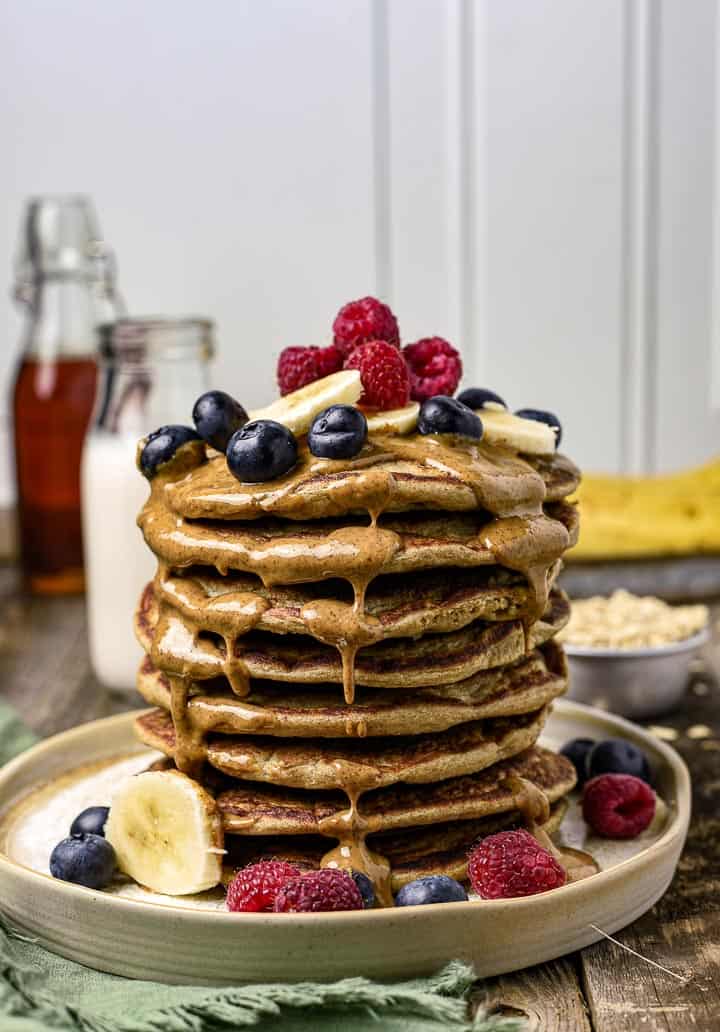 Blender pancakes stacked and covered in almond butter with blueberries, bananas, and raspberries.
