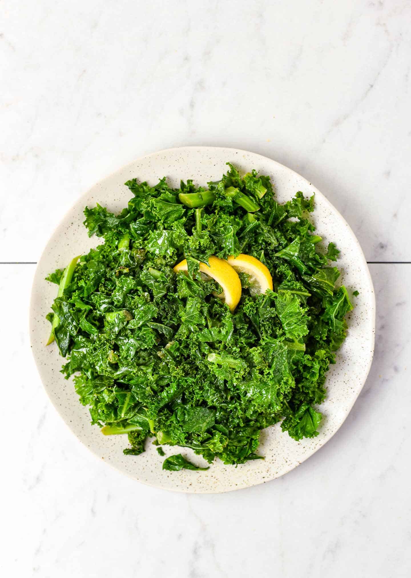 Sauteed kale on plate with lemon wedges.
