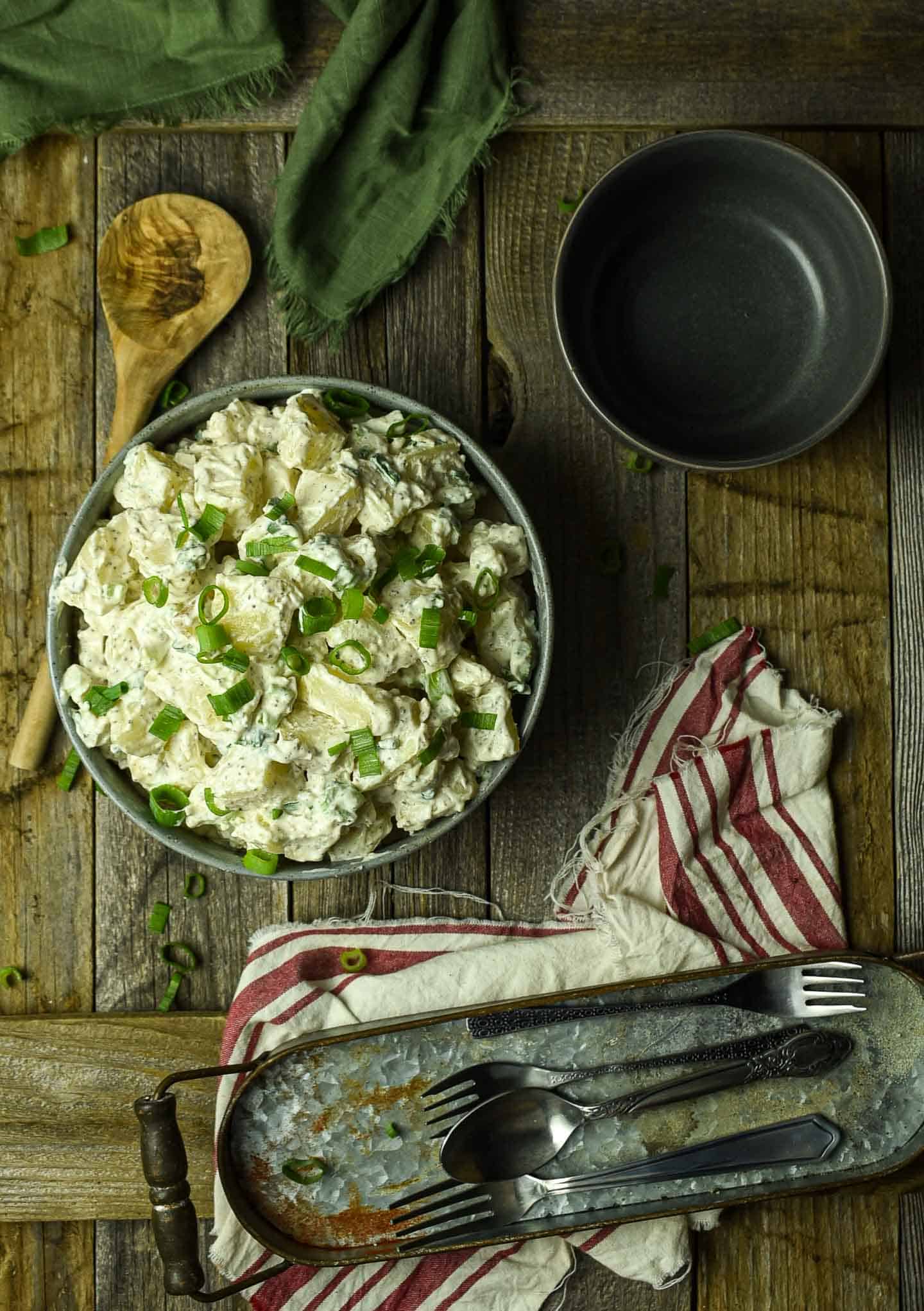 Potato salad on table with empty bowl and forks and spoonl