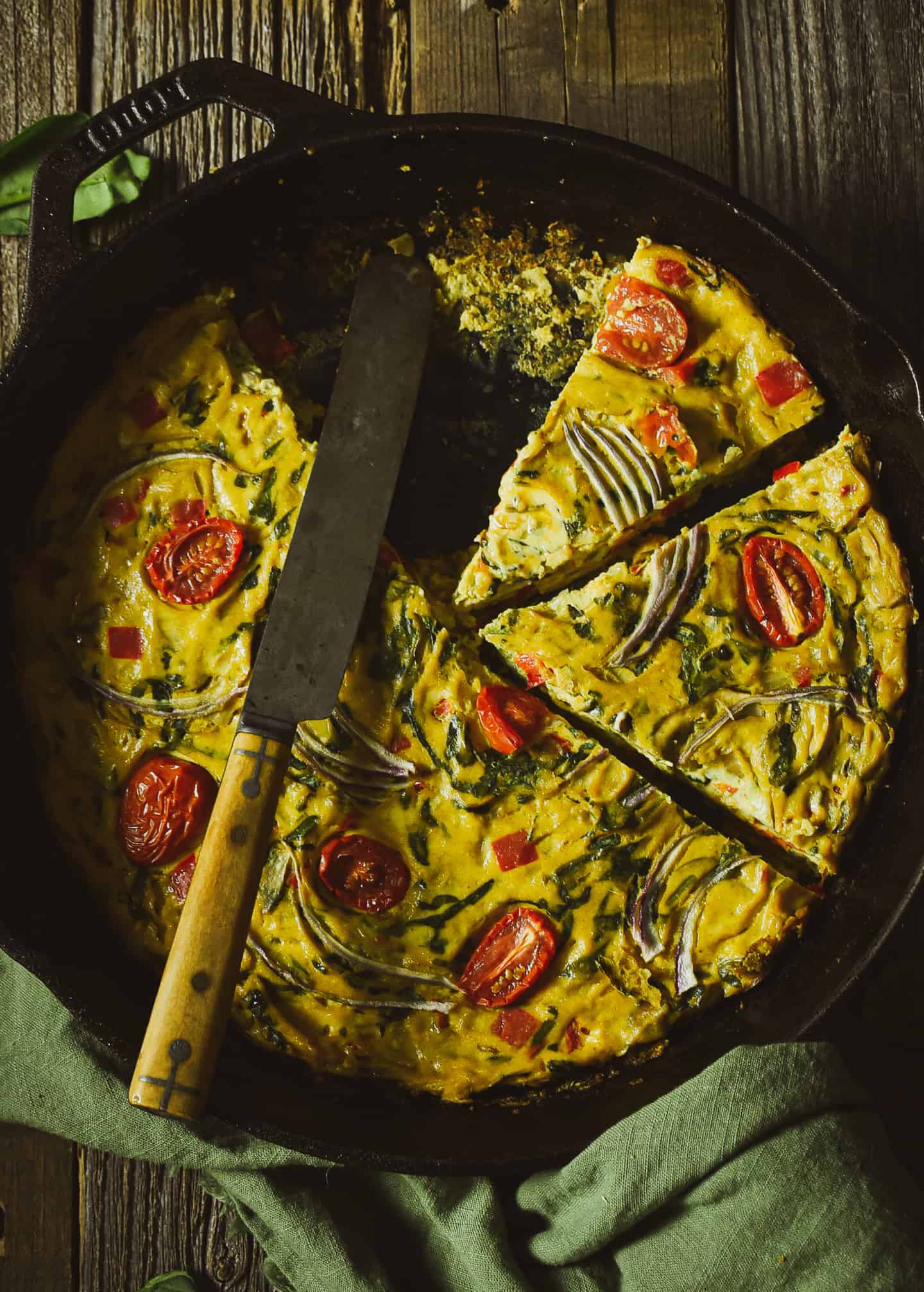 Two slices of vegetarian frittata in cast iron skillet with knife.