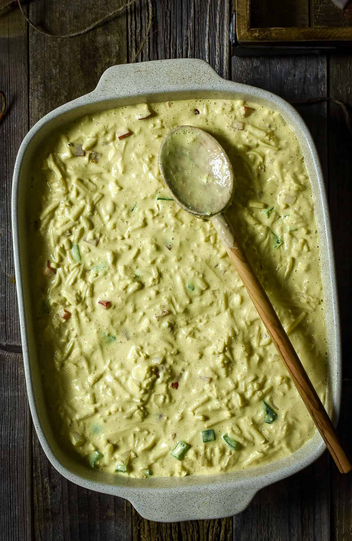 Breakfast casserole ingredients in a baking dish with wooden spoon on top.