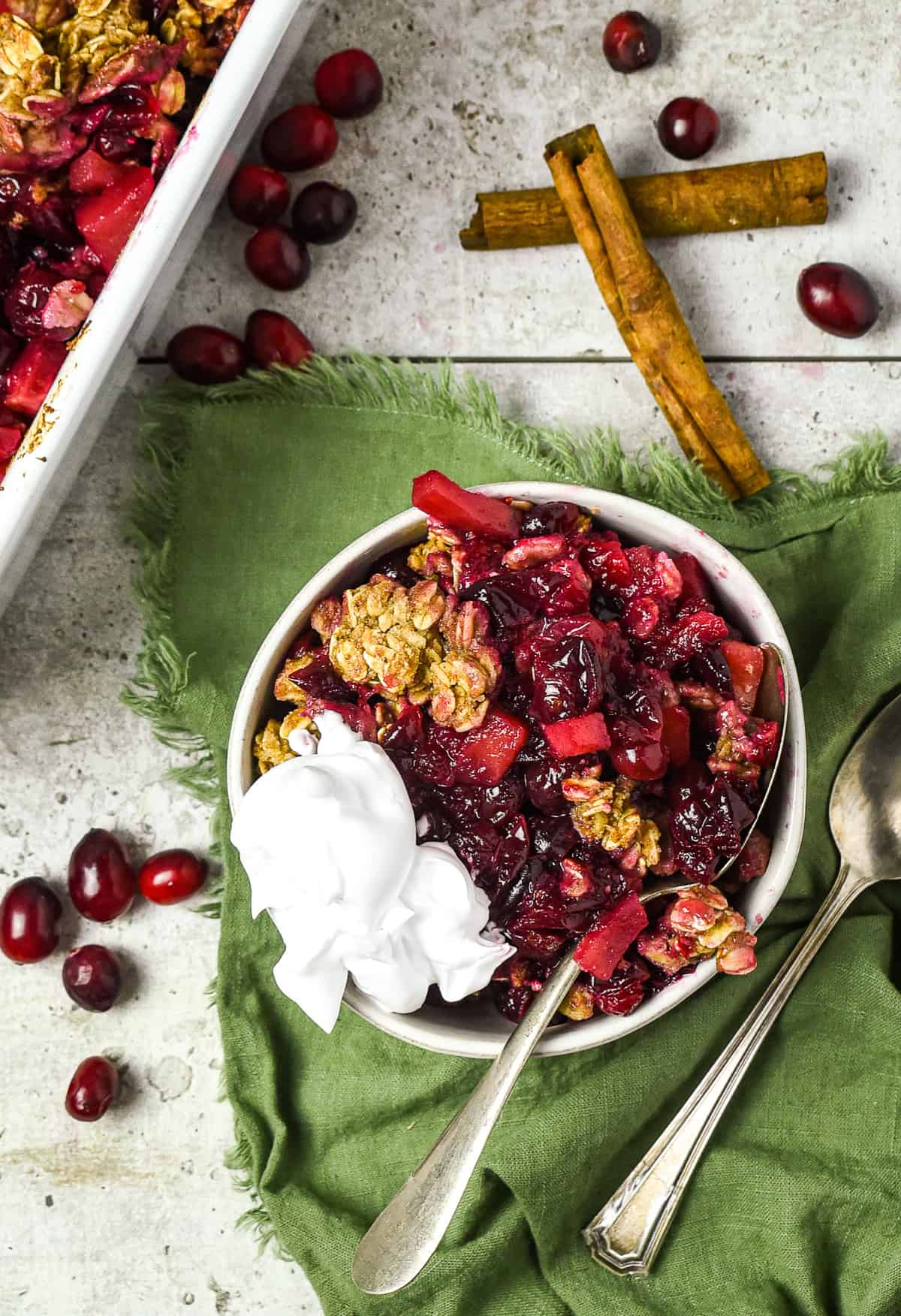 Bowl of apple cranberry crisp with vegan whipped cream.