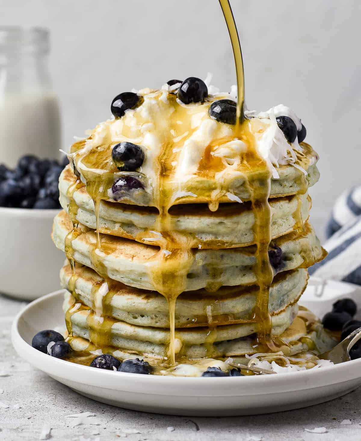 vegan blueberry pancakes on plate with maple syrup, whipped cream, and blueberries.