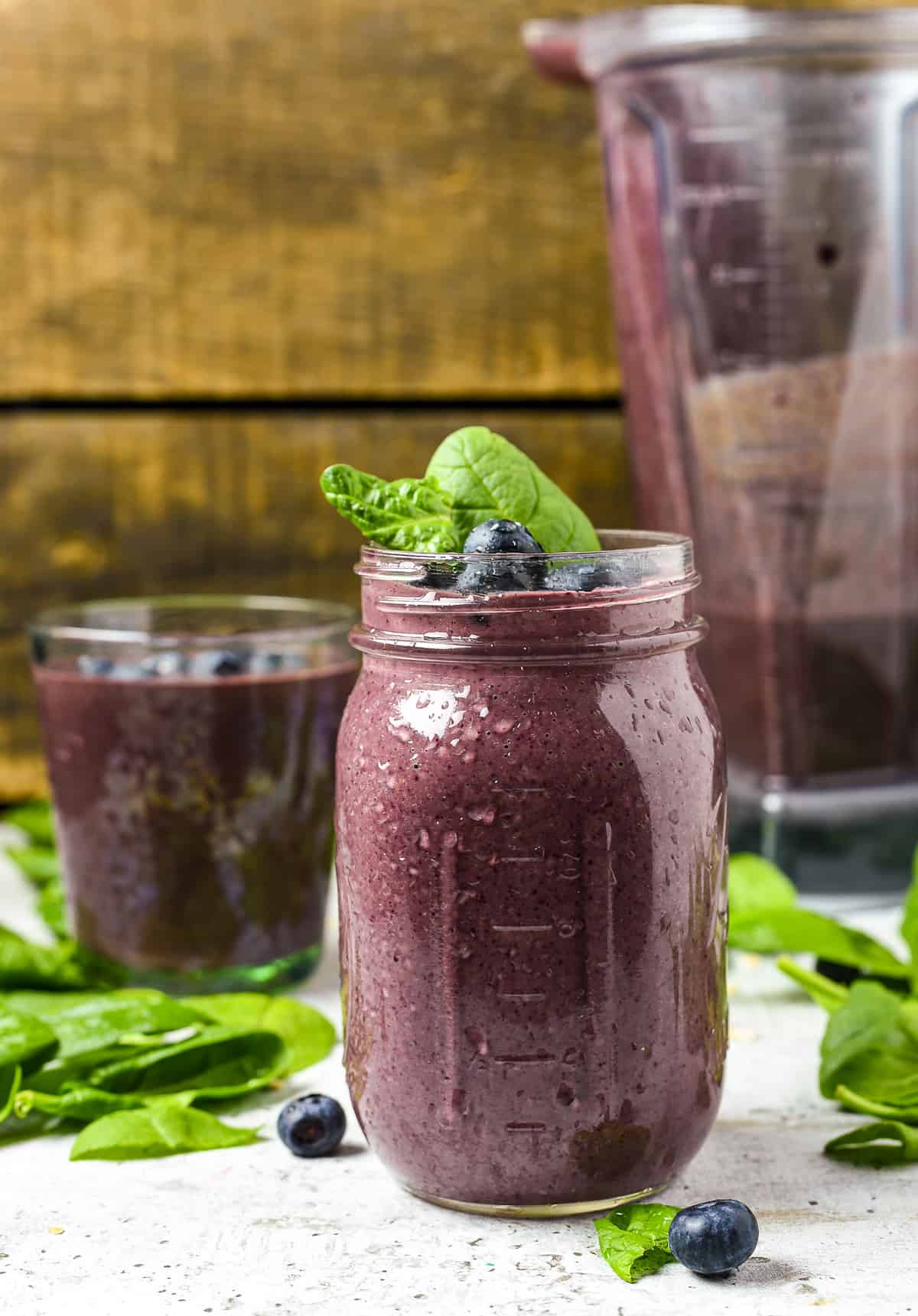 Spinach berry smoothie with vitamix pitcher on table with spinach.