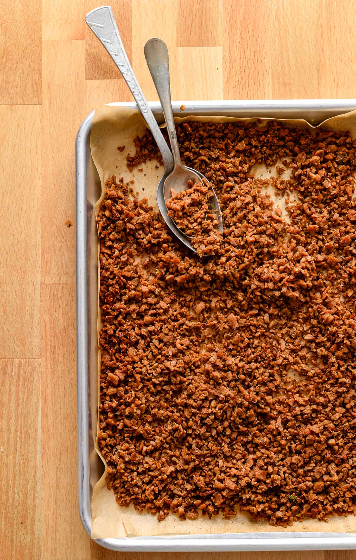 veggie sausage crumbles on baking sheet with two spoons.