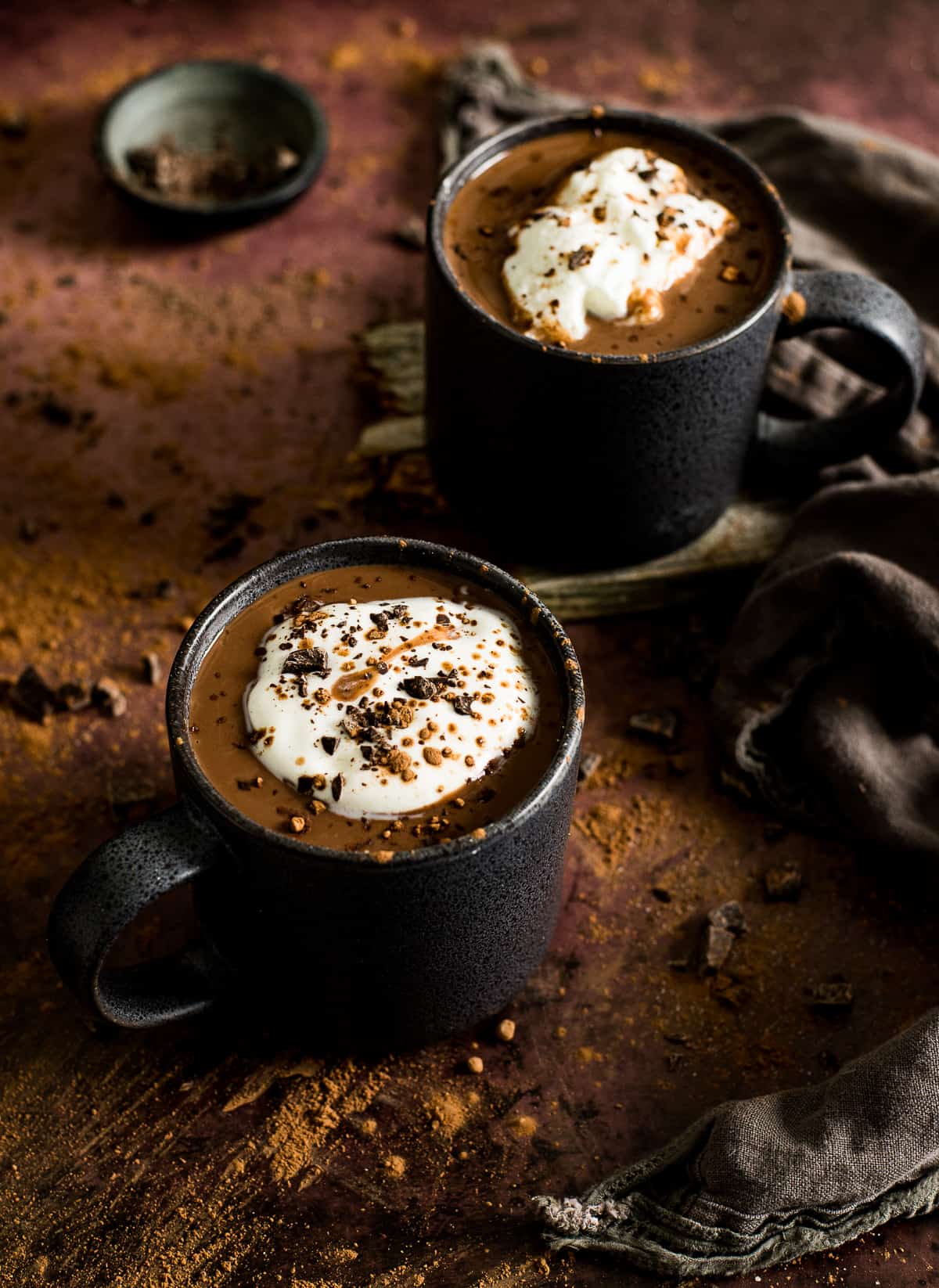 Two cups of vegan hot chocolate with whipped cream and chocolate shavings.