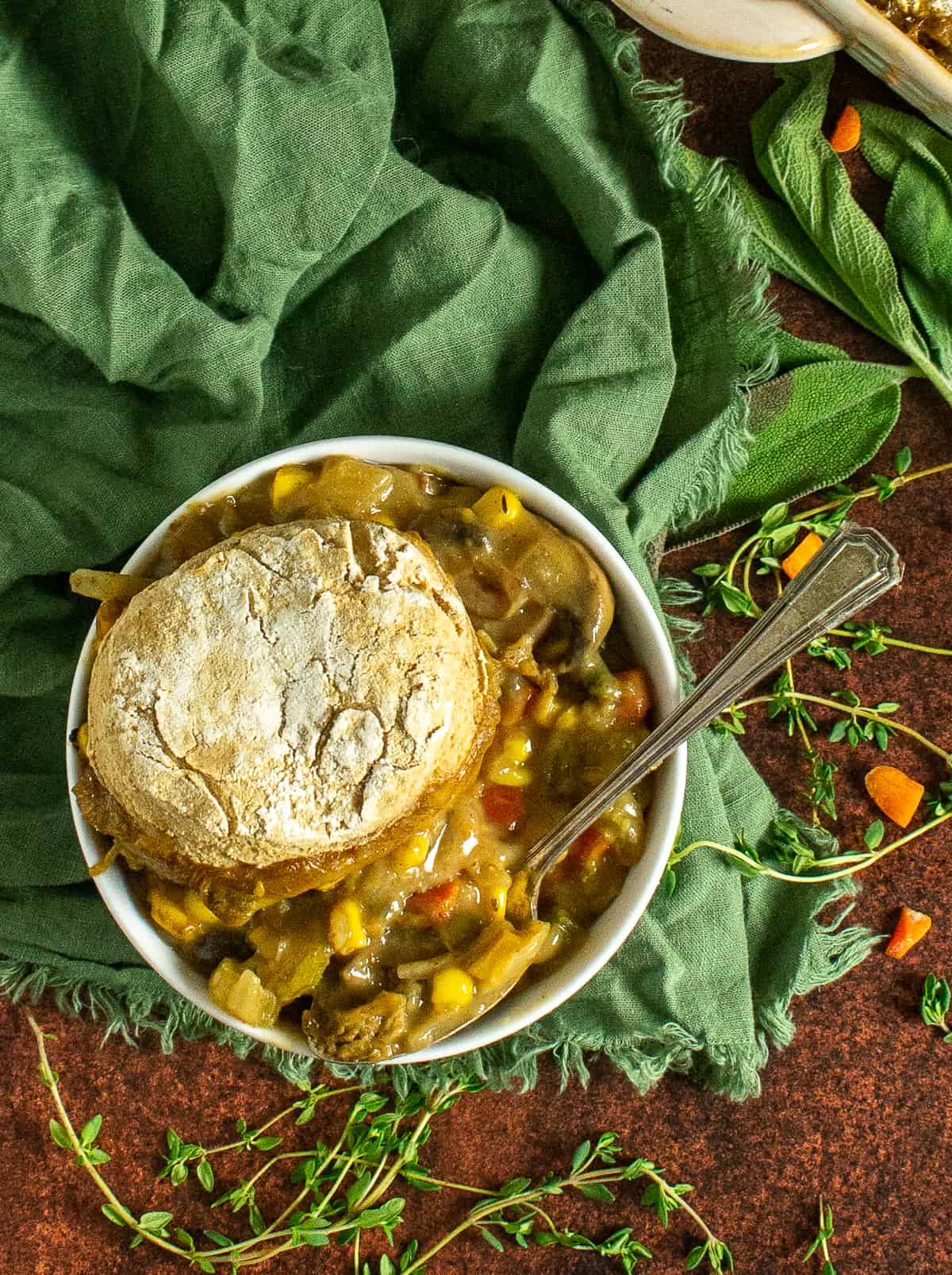 Vegetable pot pie with biscuit in bowl with spoon.