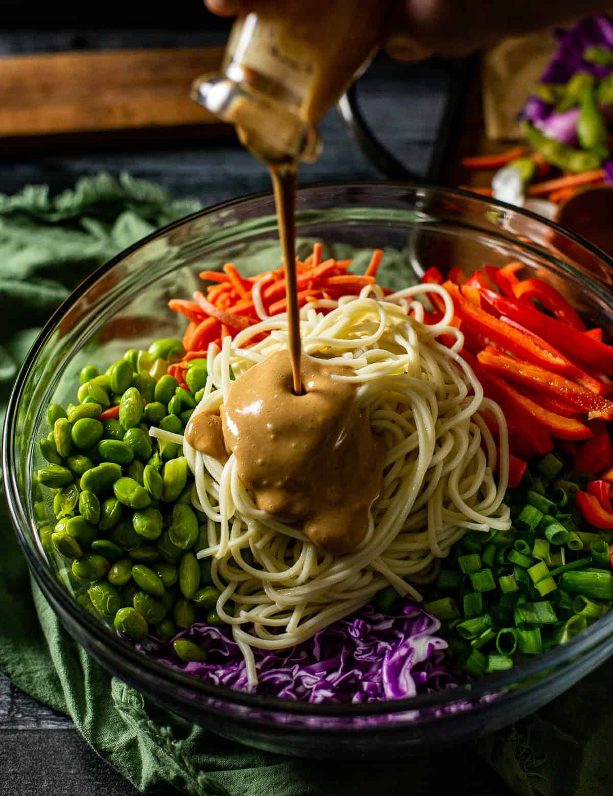 peanut sauce being poured over veggies and noodles in bowl