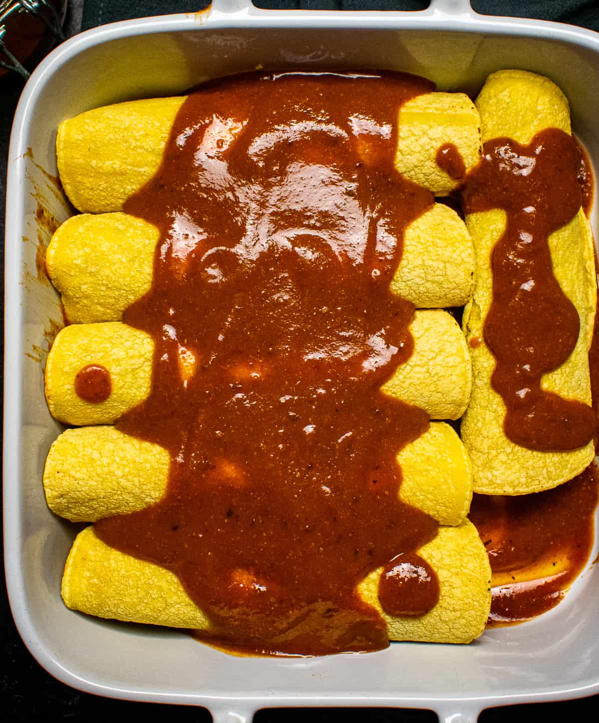 Enchiladas with sauce in baking dish.