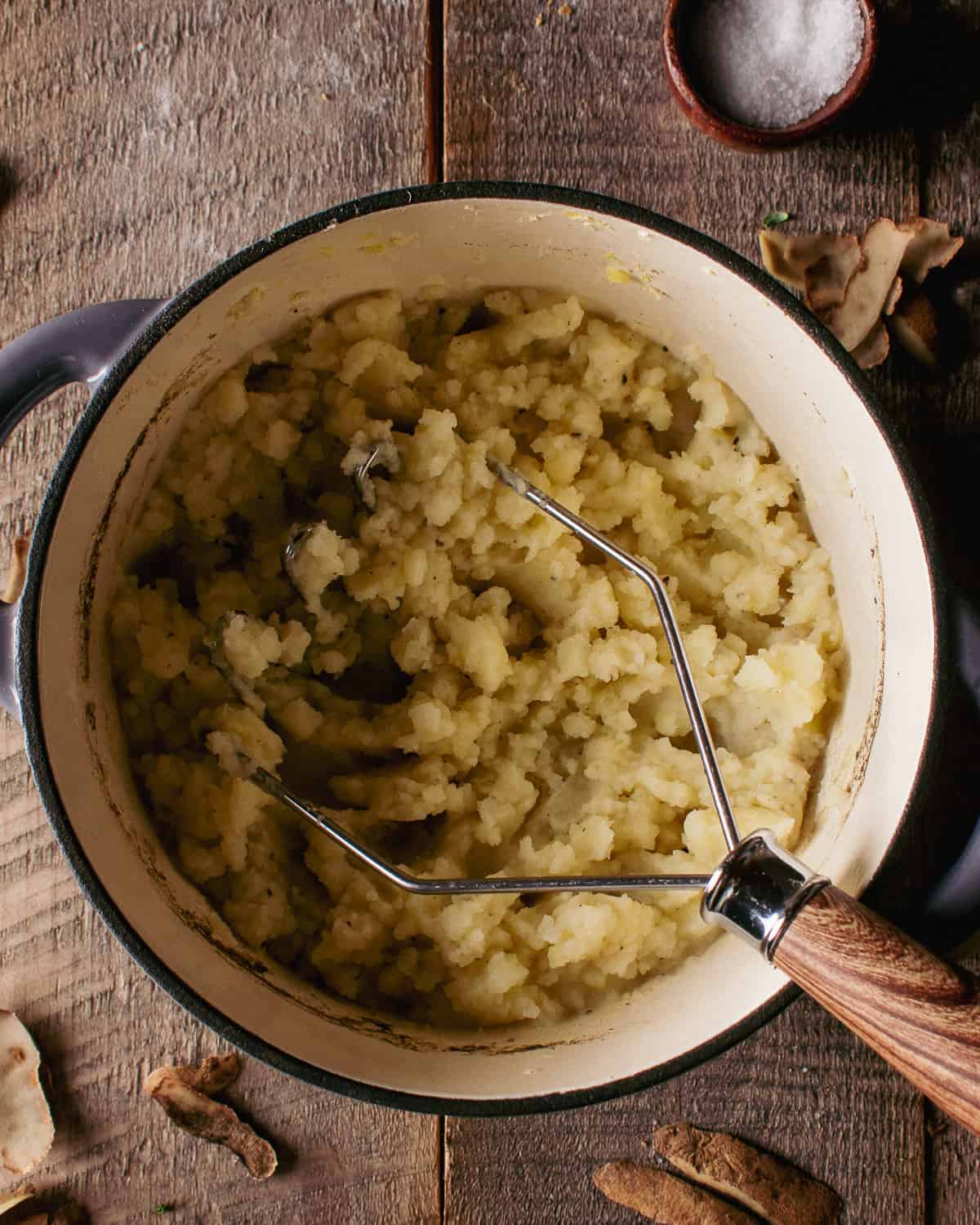 mashed potatoes in pot with potato masher.