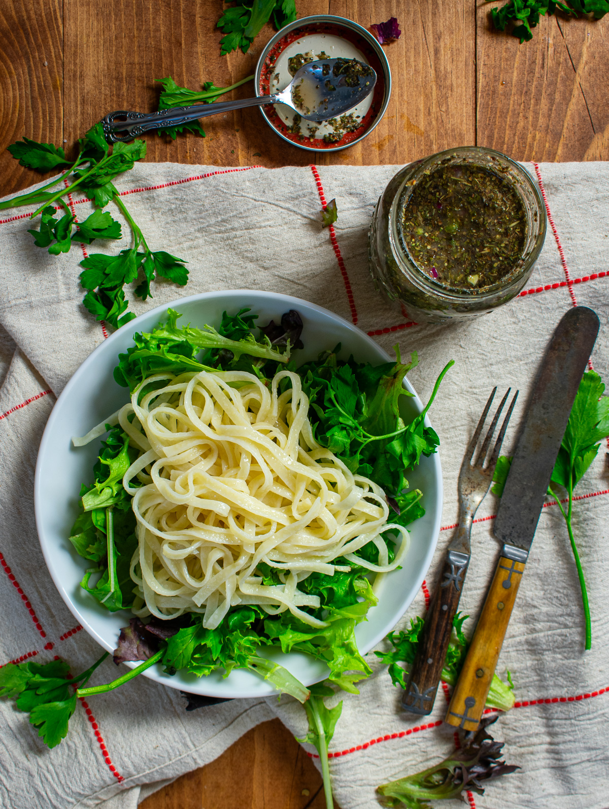 Italian dressing in jar with greens and pasta in bowl.