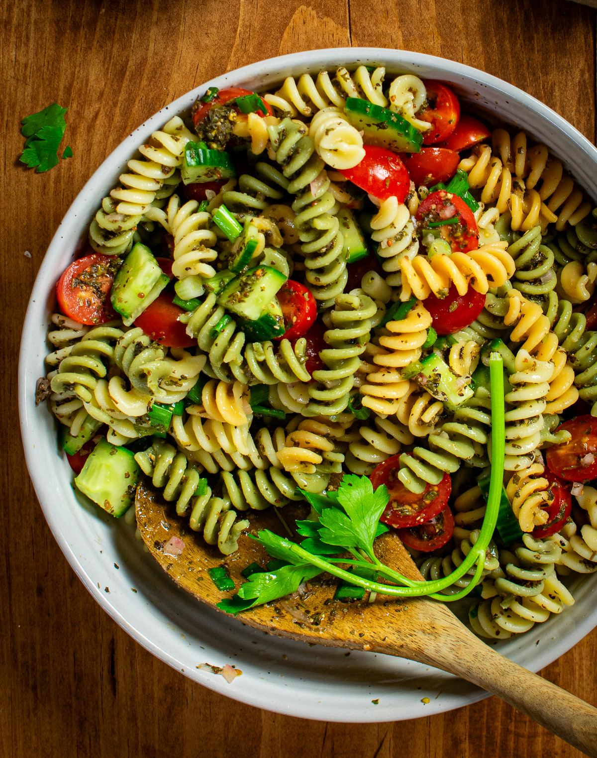 Pasta salad in mixing bowl with wooden spoon.